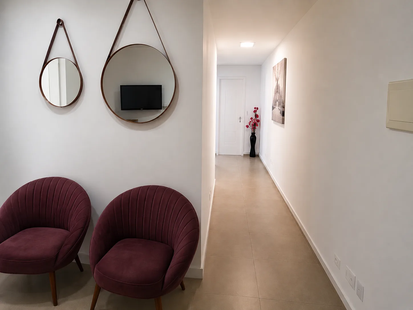 Recepção com poltronas vinho, espelhos redondos com molduras marrons e flores vermelhas