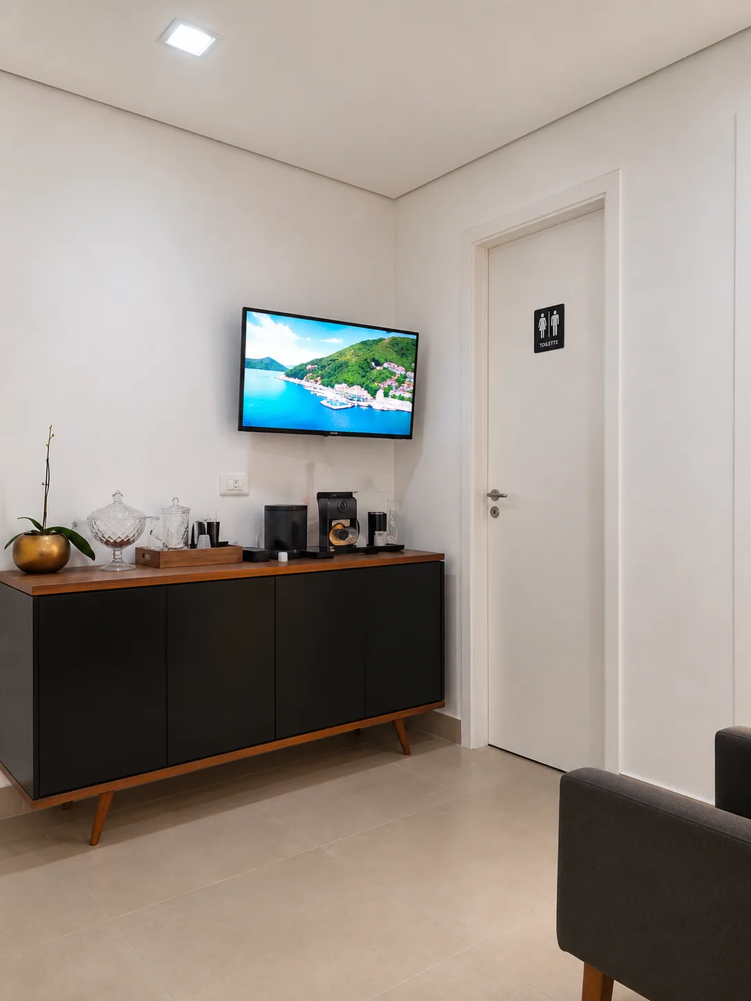 Recepção com móveis em preto e madeira, TV na parede e plantas decorativas em ambiente moderno e acolhedor